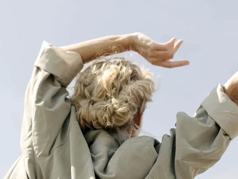 Woman with light-colored hair raises her arms beneath a clear, bright sky. Symbolic image representing the ellexx equity investment product.